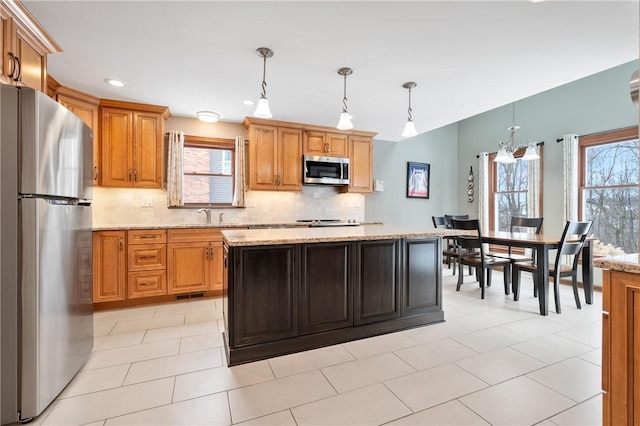 kitchen featuring tasteful backsplash, light stone counters, hanging light fixtures, appliances with stainless steel finishes, and a kitchen island