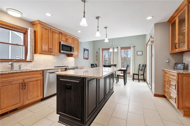 kitchen featuring a kitchen island, appliances with stainless steel finishes, sink, hanging light fixtures, and light stone countertops