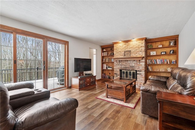 living room with built in shelves, a fireplace, a textured ceiling, and light wood-type flooring