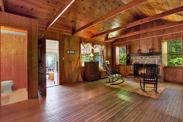 sitting room with beam ceiling, wooden walls, a stone fireplace, wooden ceiling, and light wood-type flooring