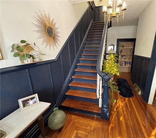 stairway with parquet floors and an inviting chandelier