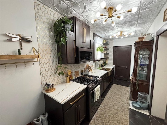 kitchen with black gas range oven, an inviting chandelier, dark brown cabinetry, dark tile patterned flooring, and decorative backsplash