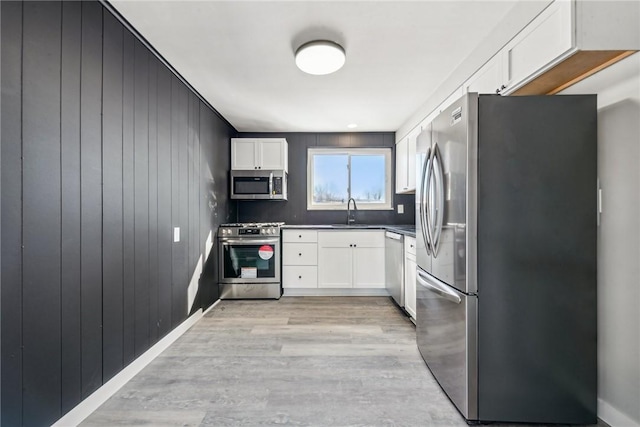 kitchen with white cabinetry, wood walls, and appliances with stainless steel finishes