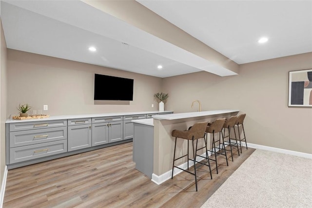 bar featuring light hardwood / wood-style flooring, sink, beam ceiling, and gray cabinets