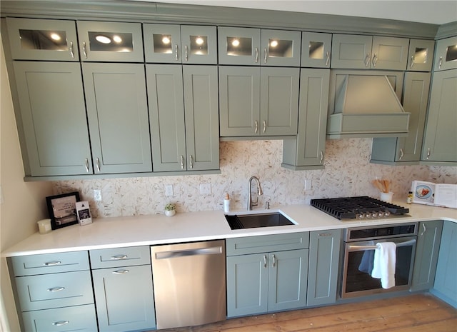 kitchen with appliances with stainless steel finishes, sink, backsplash, green cabinetry, and custom range hood