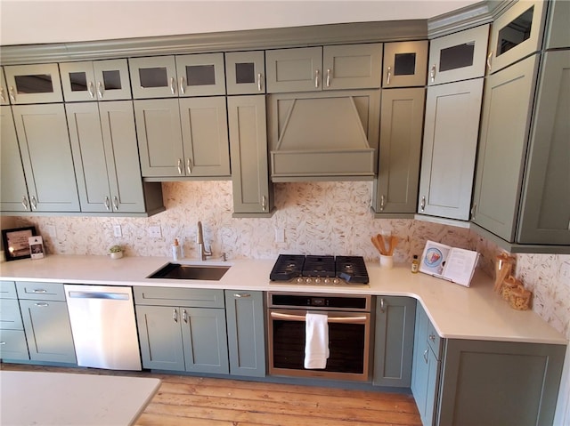 kitchen featuring sink, tasteful backsplash, light hardwood / wood-style flooring, appliances with stainless steel finishes, and custom range hood