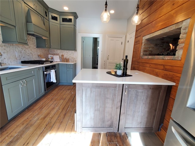 kitchen with decorative light fixtures, tasteful backsplash, light hardwood / wood-style floors, stainless steel appliances, and custom range hood