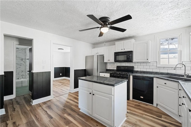 kitchen with tasteful backsplash, sink, white cabinets, a center island, and black appliances