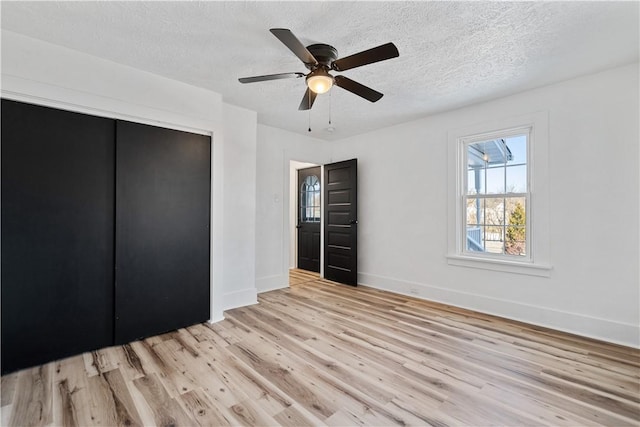 unfurnished bedroom with a textured ceiling, a closet, ceiling fan, and light wood-type flooring