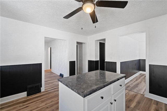 kitchen with hardwood / wood-style floors, a textured ceiling, white cabinets, and ceiling fan