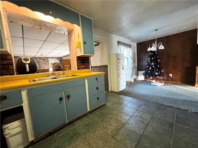 kitchen with sink, wooden walls, dark colored carpet, green cabinetry, and decorative light fixtures