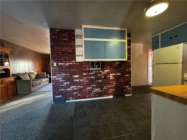 kitchen featuring white refrigerator, wooden walls, and dark colored carpet