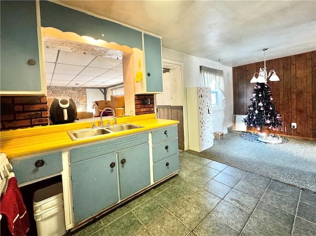 kitchen with wood walls, sink, a chandelier, hanging light fixtures, and green cabinetry