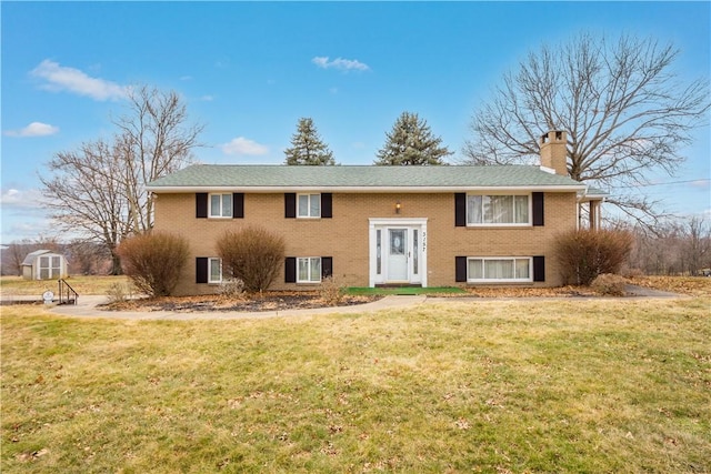 split foyer home with an outbuilding, brick siding, a chimney, a storage unit, and a front yard