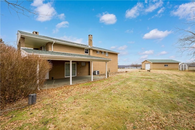 rear view of house featuring a lawn, an outbuilding, a storage unit, a patio area, and brick siding