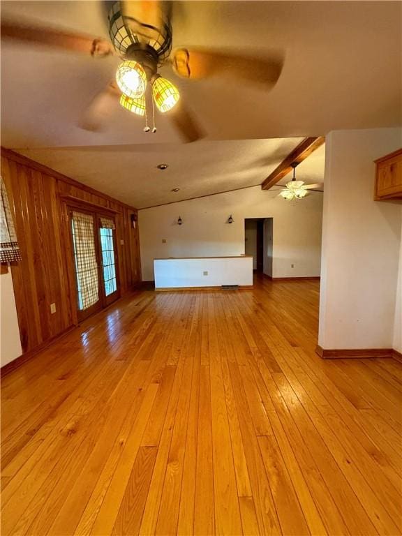 unfurnished living room featuring light wood-type flooring, ceiling fan, lofted ceiling with beams, and wood walls