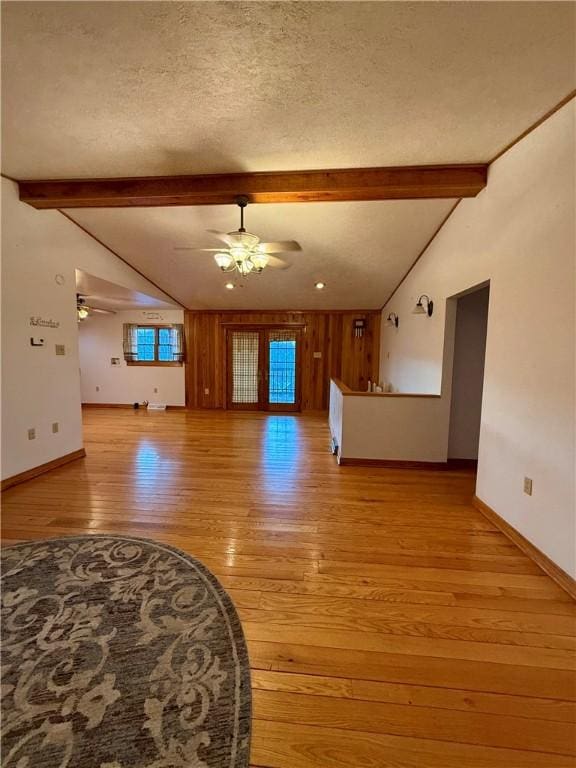 unfurnished living room featuring vaulted ceiling with beams, a textured ceiling, ceiling fan, and light hardwood / wood-style flooring