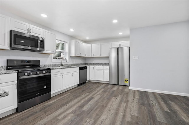 kitchen with sink, dark wood-type flooring, appliances with stainless steel finishes, light stone countertops, and white cabinets