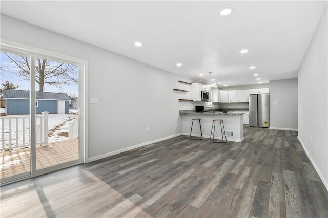 kitchen with dark hardwood / wood-style floors, a breakfast bar area, white cabinets, kitchen peninsula, and stainless steel appliances