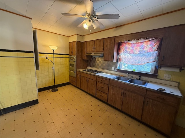 kitchen featuring sink, ceiling fan, tile walls, stainless steel gas cooktop, and oven