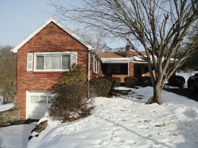 snow covered facade featuring brick siding and an attached garage