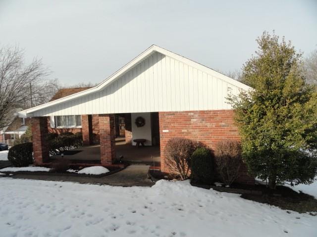 view of snow covered exterior with brick siding and a patio area