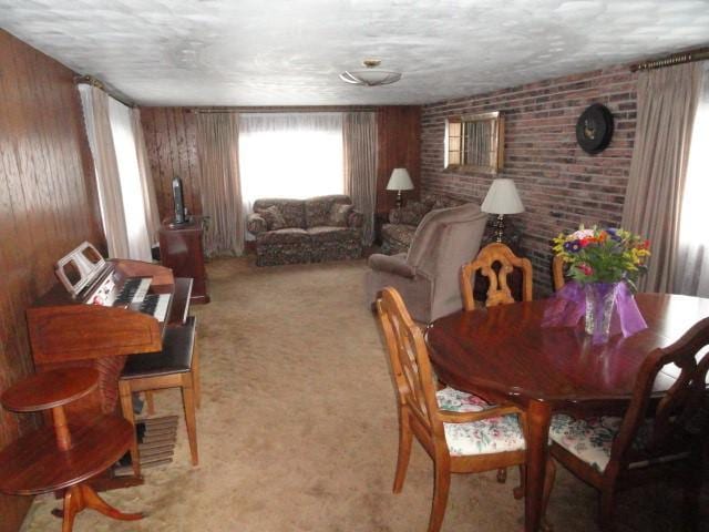 dining room with wooden walls, a textured ceiling, light colored carpet, and brick wall