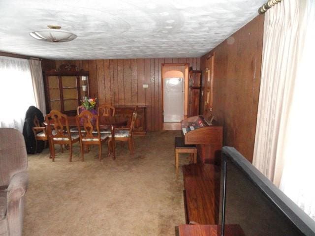 dining area with a textured ceiling, wood walls, and light colored carpet