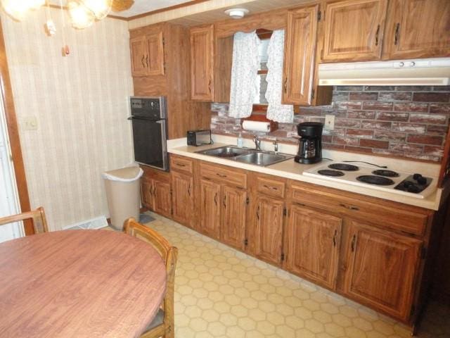kitchen with a sink, white electric cooktop, light countertops, under cabinet range hood, and wall oven