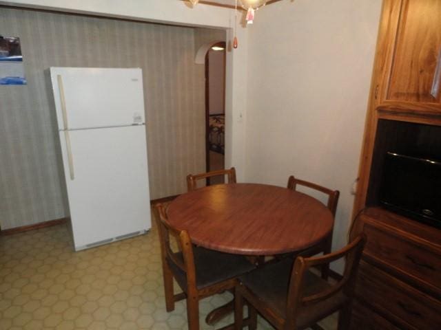 dining room featuring arched walkways, light floors, and wallpapered walls