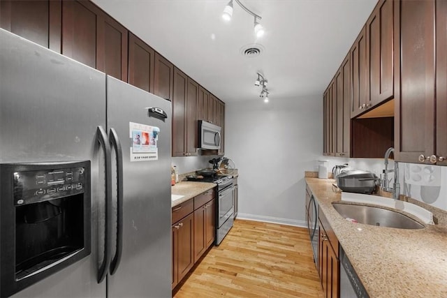 kitchen featuring light stone counters, stainless steel appliances, sink, and light hardwood / wood-style flooring