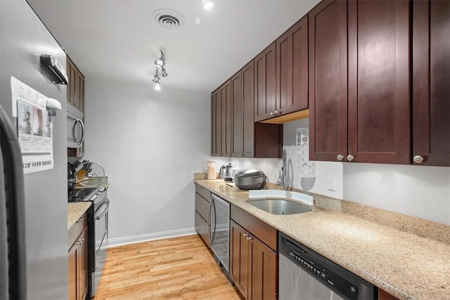 kitchen with sink, rail lighting, stainless steel appliances, light stone countertops, and light wood-type flooring