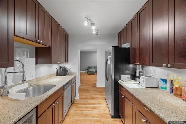 kitchen with light stone countertops, appliances with stainless steel finishes, sink, and light hardwood / wood-style flooring