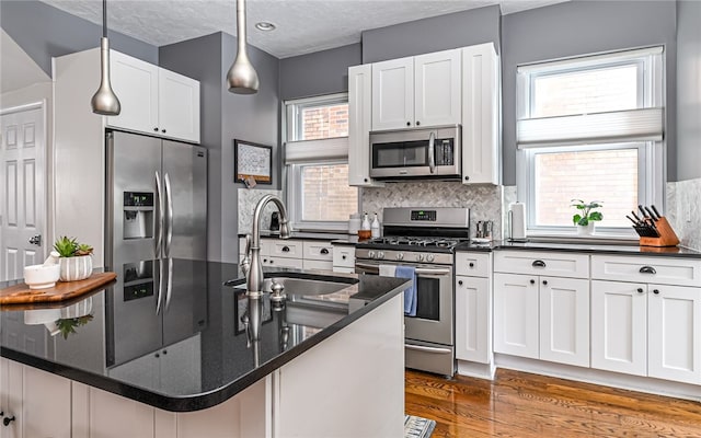 kitchen with sink, white cabinetry, dark stone countertops, pendant lighting, and stainless steel appliances