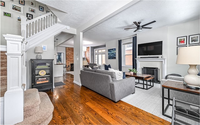 living room featuring dark hardwood / wood-style floors, ceiling fan, a fireplace, and a textured ceiling