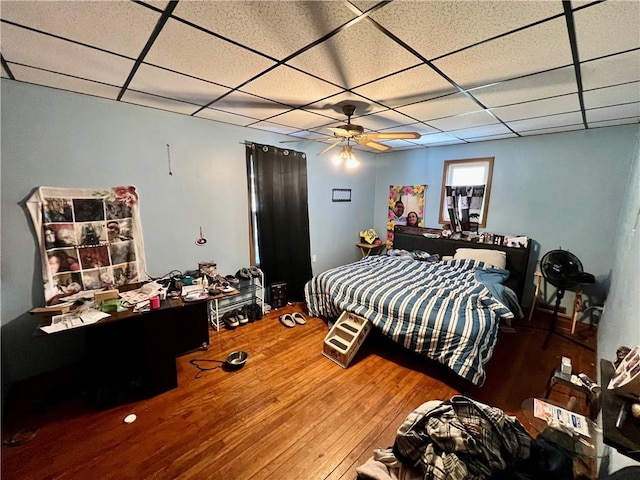 bedroom featuring hardwood / wood-style flooring, ceiling fan, and a drop ceiling