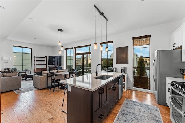 kitchen with appliances with stainless steel finishes, an island with sink, sink, white cabinets, and light hardwood / wood-style flooring