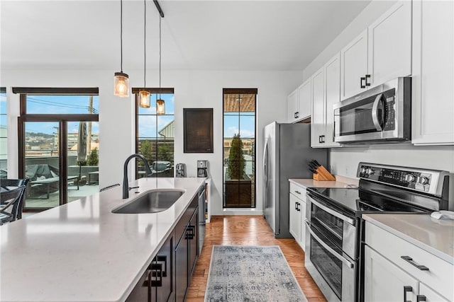 kitchen featuring sink, light wood-type flooring, an island with sink, stainless steel appliances, and white cabinets