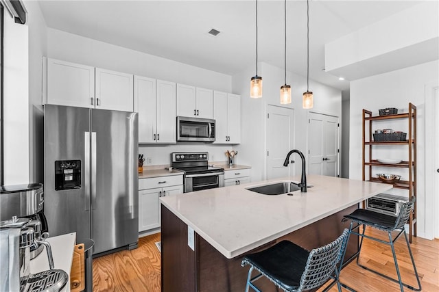 kitchen with sink, decorative light fixtures, appliances with stainless steel finishes, a kitchen island with sink, and white cabinets