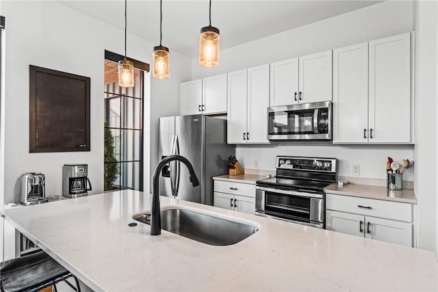 kitchen featuring sink, appliances with stainless steel finishes, white cabinetry, hanging light fixtures, and a kitchen bar