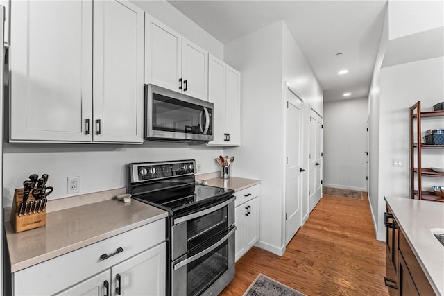 kitchen featuring white cabinetry, light hardwood / wood-style flooring, light stone countertops, and appliances with stainless steel finishes