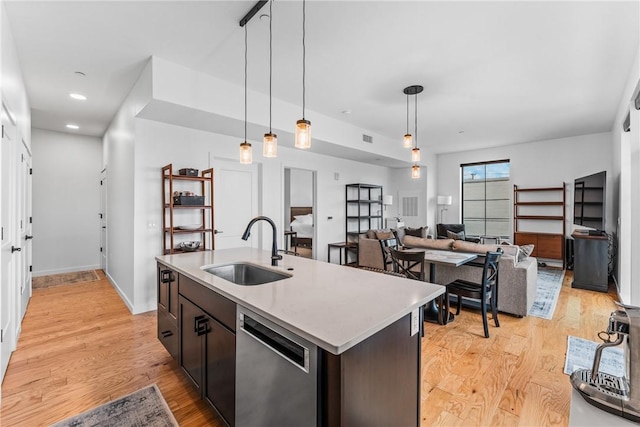 kitchen featuring pendant lighting, dishwasher, sink, a kitchen island with sink, and light hardwood / wood-style flooring