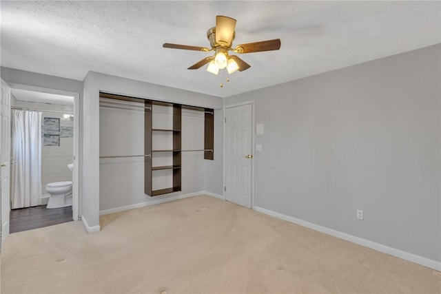 unfurnished bedroom featuring light carpet, a textured ceiling, ensuite bath, and ceiling fan