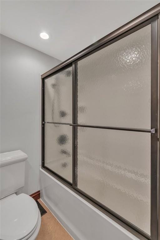 bathroom featuring toilet, bath / shower combo with glass door, and tile patterned flooring