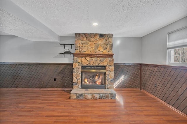 unfurnished living room with hardwood / wood-style flooring, a fireplace, wooden walls, and a textured ceiling