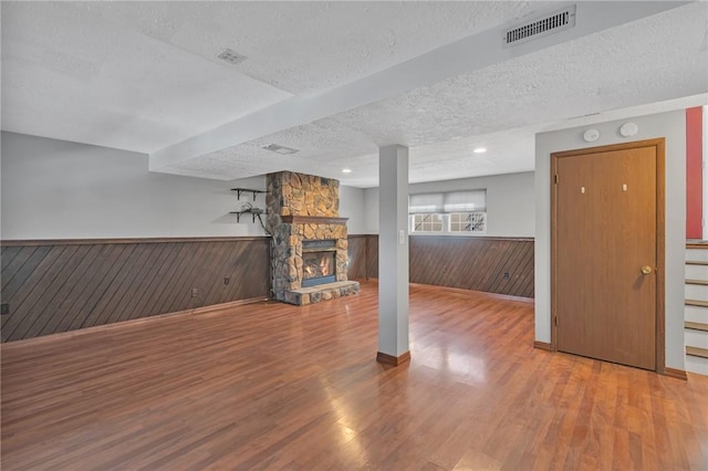 unfurnished living room with wood-type flooring, a stone fireplace, a textured ceiling, and wood walls