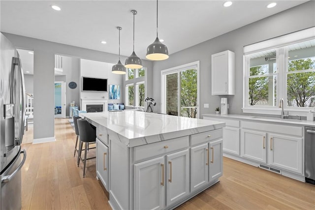 kitchen with sink, white cabinetry, stainless steel appliances, a kitchen island, and decorative light fixtures