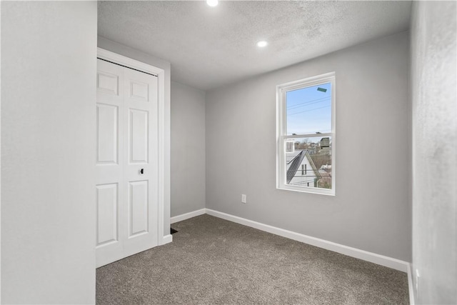 unfurnished bedroom featuring dark colored carpet, a textured ceiling, and a closet