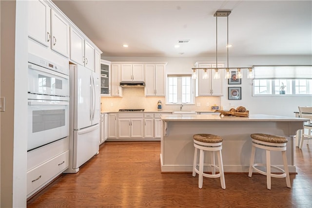 kitchen with white cabinetry, white appliances, decorative light fixtures, and a kitchen island