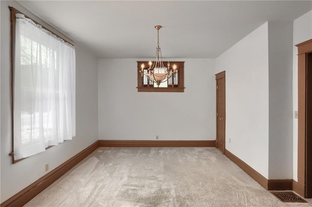 empty room with an inviting chandelier, light colored carpet, and a healthy amount of sunlight